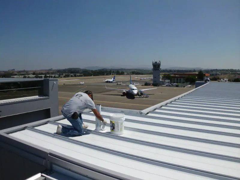 Worker applying paint to an airport rooftop surface