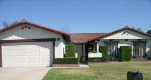A white house with red tile roof and two garage doors.