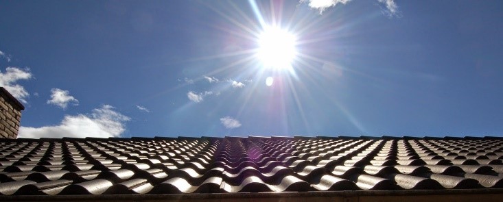 A sun shining over the sky with a roof in the foreground.