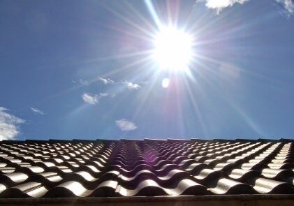 A sun shining over the sky with a roof in the foreground.